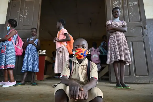 A young boy wearing a face mask sits outside his classroom at a primary school in Abidjan