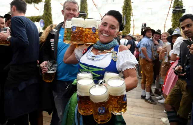 A woman smiles as she carries beer at the opening day of the 186th Oktoberfest in Munich, Germany, 21 September, 2019