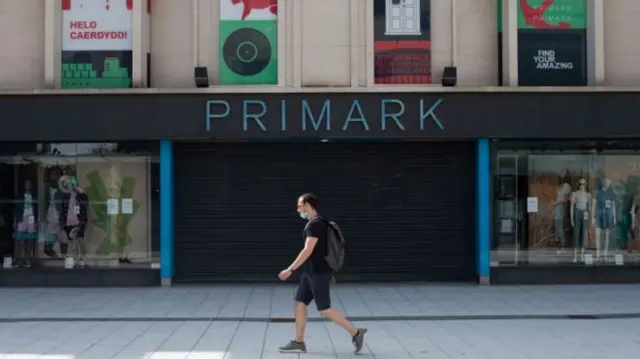 A man in a mask walking past a branch of Primark