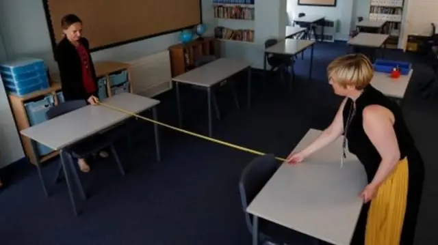 Two members of staff measure out a 2m distance in a school classroom