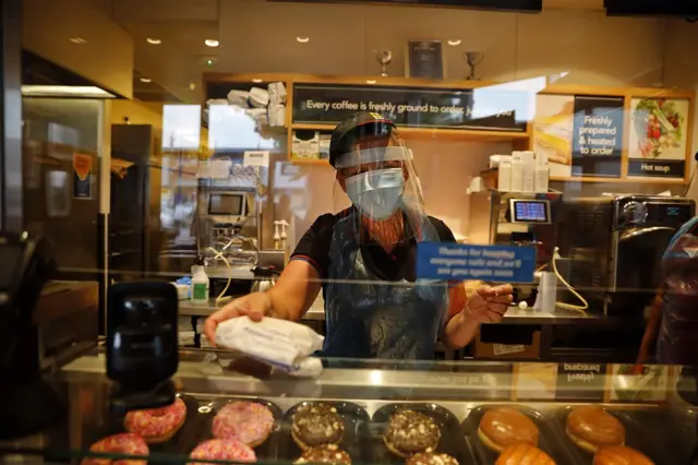 An employee wearing PPE including a mask and visor serves at the counter of a Greggs bakery in London on June 18, 2020 after the chain reopened hundreds of stores around the UK following their coronavirus shutdown.