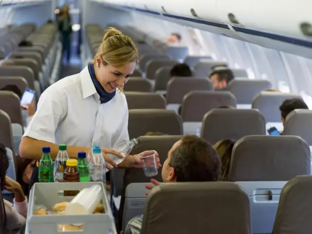 An airline hostess pours a drink