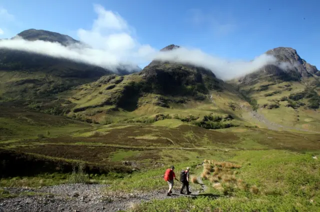 Two walkers approach the Three Sisters of Glencoe