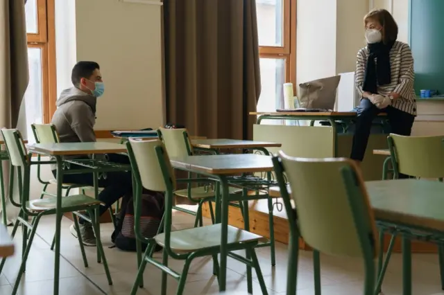 A student wearing a face covering listens to a teacher