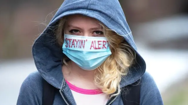 Woman in a mask which says "stay alert"