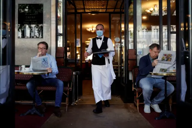 A waiter in a face mask serves customers outside a Parisian cafe