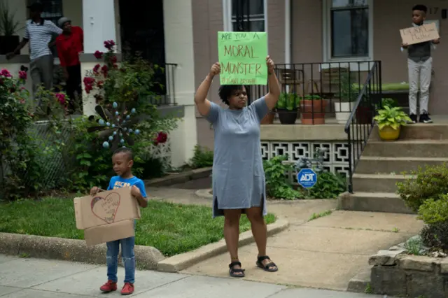 A woman and her young son hold up signs saying "Are you a moral monster" as Trump's motorcade drives past (2 June 2020)