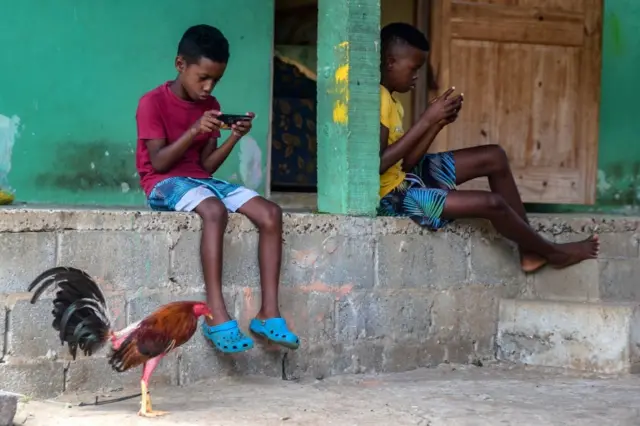 Children play on cell phones at Pedro Gonzalez Island, Pearl archipelago, Panama, during a food delivery for low-income families, on May 15, 2020