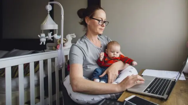 A working mother sitting at a laptop with a baby on her lap