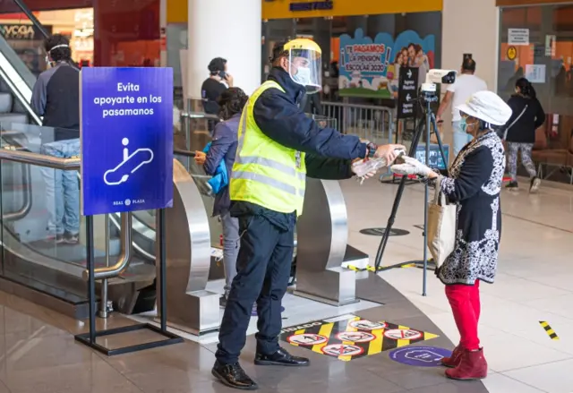 A worker gives gel alcohol to a customer inside a shopping mall in Lima on June 22, 2020