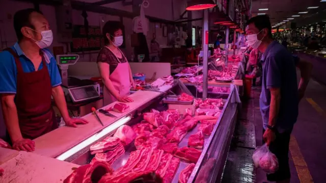 A customer (R) talks to butchers after he bought meat from their stall at a market in Beijing on June 20, 2020