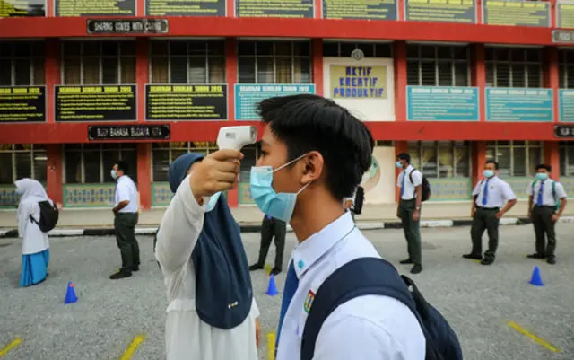 Pupils at a Malaysian high school queue to have their temperature taken