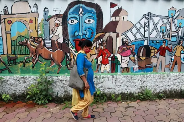 A woman wearing a mask walks past a panting of Indian art in Kolkata, India