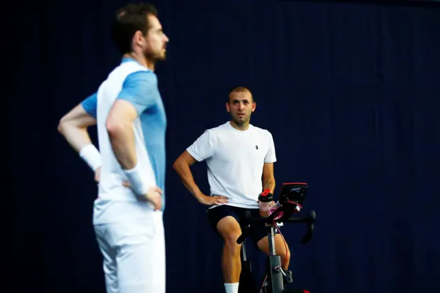 Dan Evans, on a stationary bike, looks at Andy Murray while he is not looking