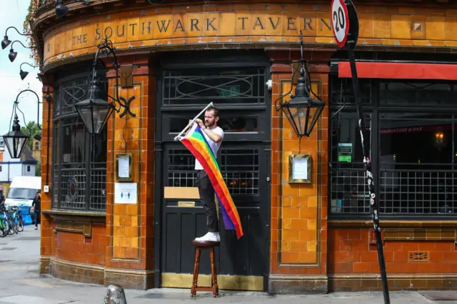 A worker hangs a rainbow flag outside The Southwark Tavern at Borough Market