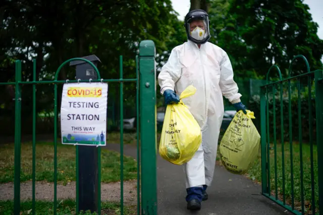 A city council worker carries rubbish from a coronavirus testing centre at Spinney Park which will be incinerated on June 29, 2020 in Leicester, England