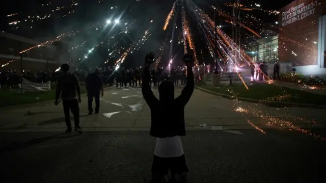 A protester stands as fireworks explode overhead in Ferguson