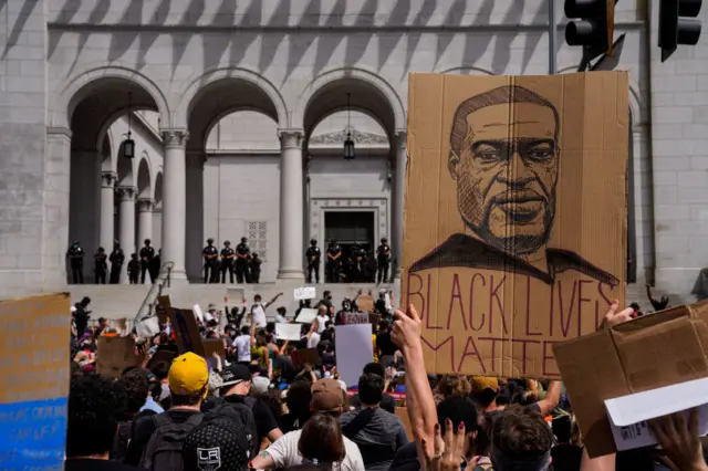 Demonstrators raise a drawing of the late George Floyd while protesting in front of LA City Hall in downtown Los Angeles on Tuesday