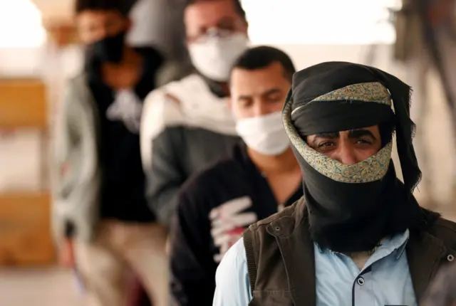 People stand in line to receive vouchers at a food distribution center supported by the World Food Program in Sanaa, Yemen June 3, 2020.