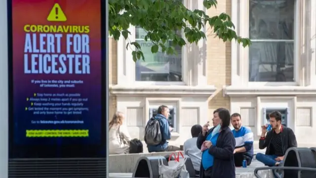 A coronavirus alert sign in Leicester with people in the background