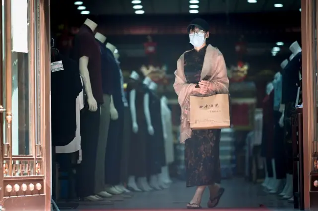 A woman wearing a face mask walks out a clothing shop in Beijing