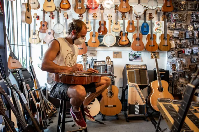 A customer wearing a protective mask plays a guitar inside a music store in Austin, Texas