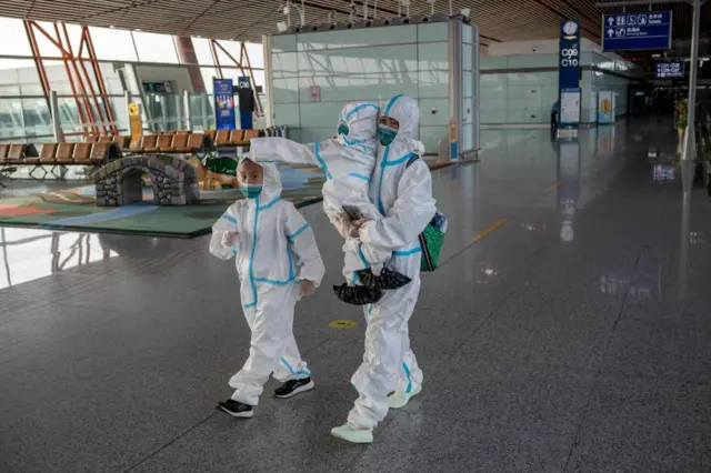 Passengers in full protective suits make their way to their gate at terminal three in Beijing's Capital International Airport