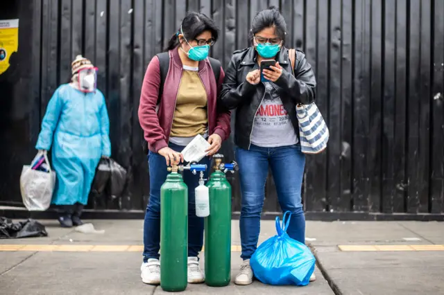 Woman stand with empty oxygen cylinders to refill them for a relative as they wait for a vehicle outside the area of respiratory diseases of the 2 de Mayo Hospital in Lima on June 3, 2020, amid the COVID-19 coronavirus pandemic.