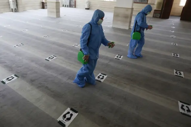 Workers wear a protective suit while spraying disinfectant in a mosque in Jordan