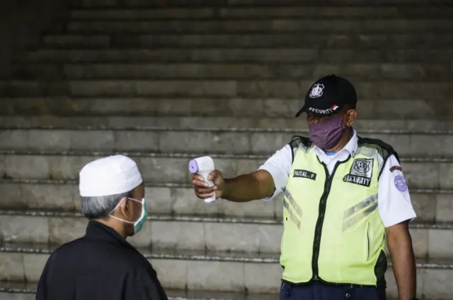 A security officer checks the body temperature of a man shortly before a Friday prayer at At-Tin mosque in Jakarta