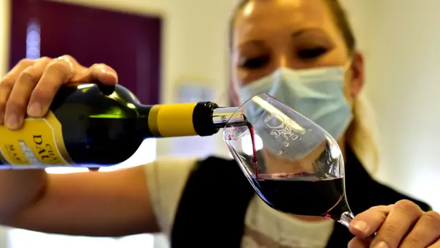 Woman wearing a mask pouring a glass of wine