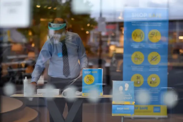 A member of staff wearing a face shield prepares a shop for reopening