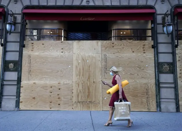 A woman walks by a boarded up Cartier store on 5th Avenue in New York City June 8, 2020