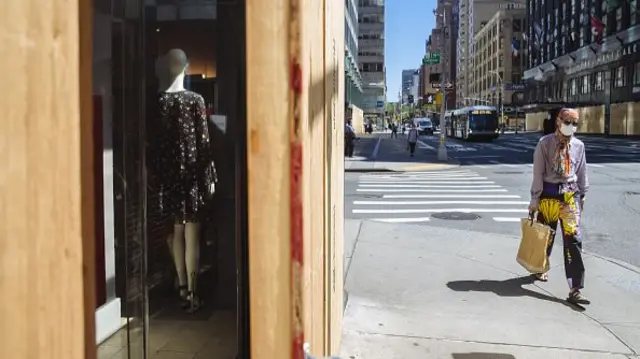 A pedestrian wearing a protective mask pass in front of a Gap Inc. Banana Republic brand store boarded up in New York