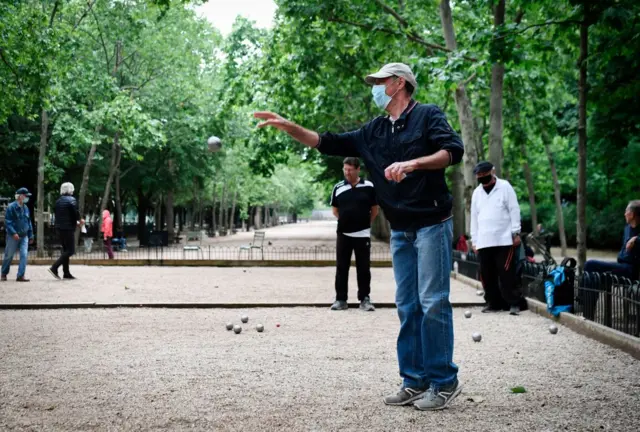 A man wearing a disposable face masks plays petanque in Paris