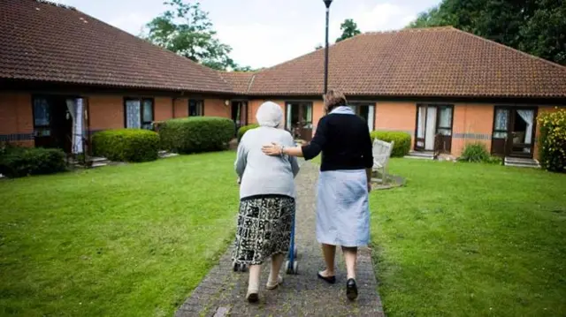 Nurse and elderly care home resident walking on a path outside