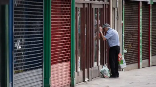 Man looks into window of shut shop on a British high street during the coronavirus pandemic