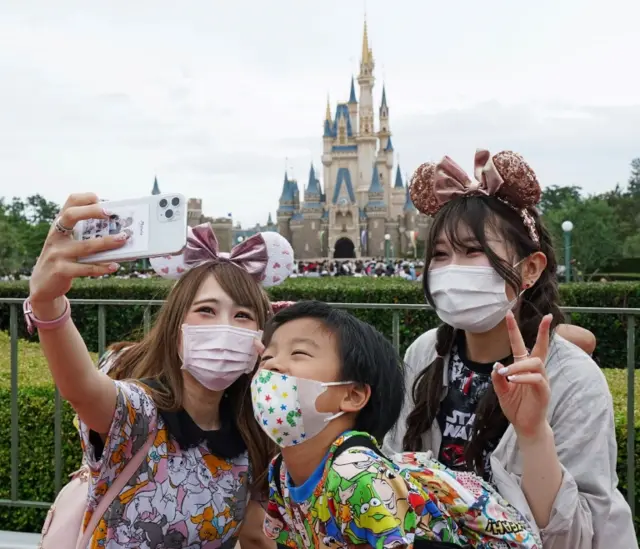 People take pictures as they arrive at Tokyo Disneyland after it reopens