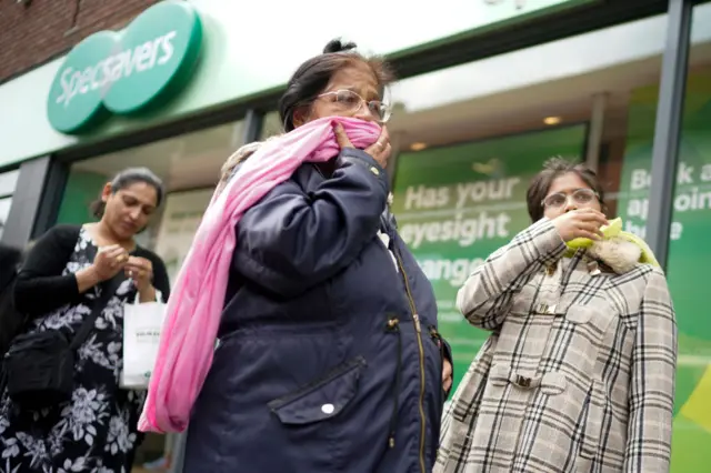 People wait outside a shop in Leicester