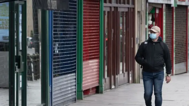 A person walking along a street with shuttered-up shops