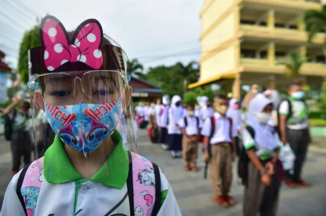 A student wearing a face shield lines up at a school in Thailand