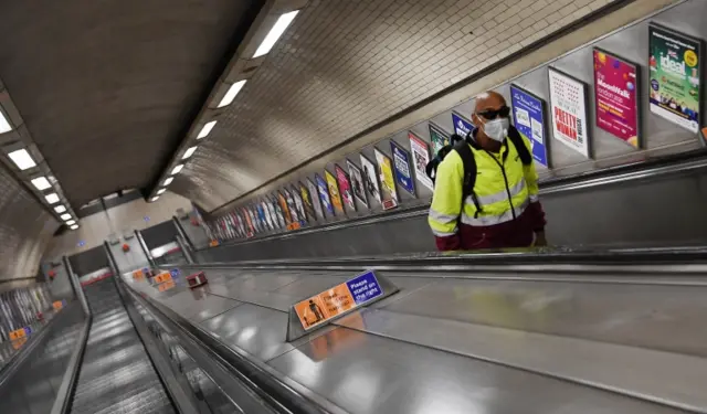 A lone commuter wearing a face mask rides up an escalator at an Underground station in London