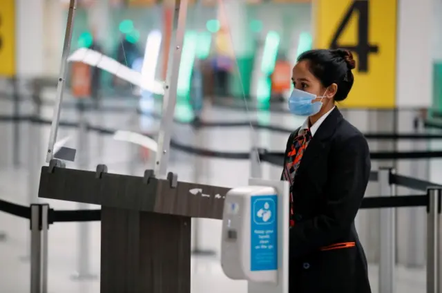 A check-in staff member waits behind a screen at Gatwick Airport,