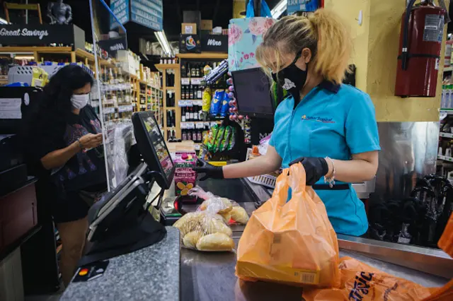 An employee at wears a protective face mask and gloves while ringing up a customer at a supermarket