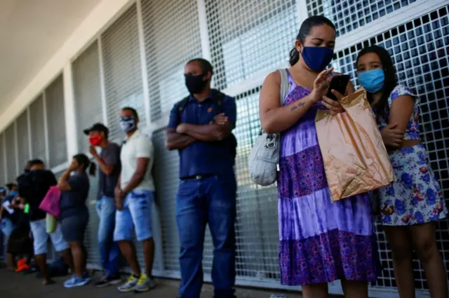 People wearing face masks wait in line in front of a public bank in Brasilia