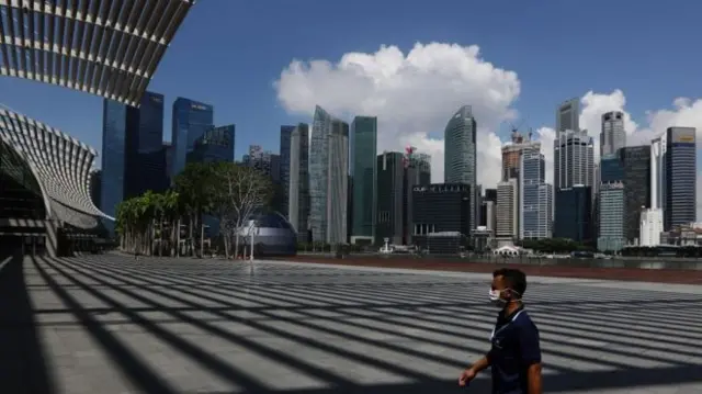 Against Singapore's skyline a man in a mask walks on a near-deserted pedestrian area in the centre of the city.