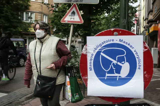 A woman wearing a face mask walks by a board bearing mask instructions in Brussels