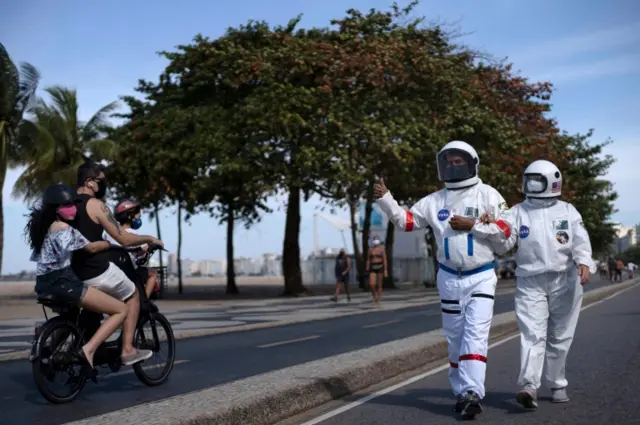 Brazilian accountant Tercio Galdino, 66, gives the thumb up to people riding a motorcycle as he and his wife Alice Galdino walk along Leme beach in protective suits