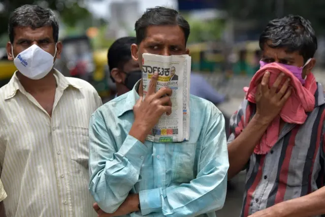 In this picture taken on July 9, 2020, a man holds a newspaper to cover his face in the absence of his facemask during the COVID-19 coronavirus pandemic, in Bangalore