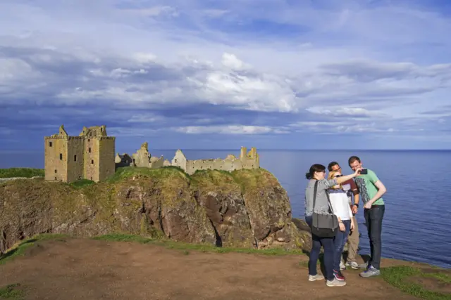 Tourists taking selfies at Dunnottar Castle, ruined medieval fortress near Stonehaven on cliff along the North Sea coast, Aberdeenshire, Scotland,